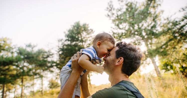 A man raises his toddler son up and presses his forehead to his son's.