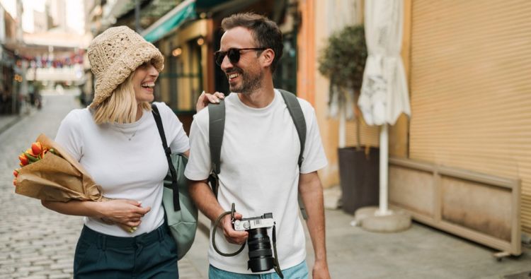 A young couple walk down a cobblestone street together on vacation.