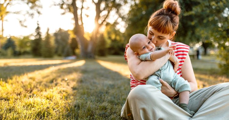 A woman gives her young toddler a big hug while sitting in the park.