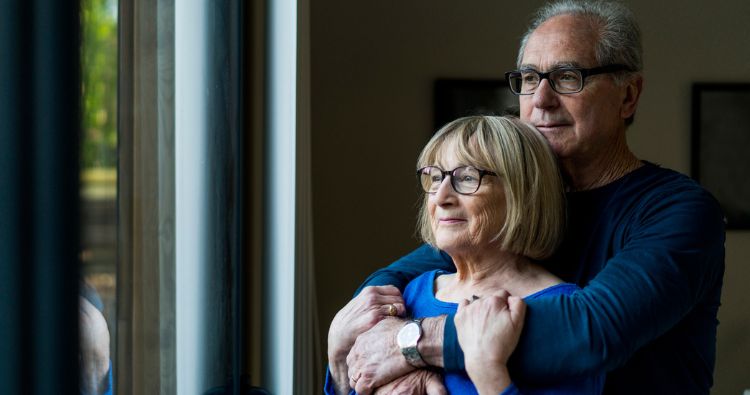 An older couple looking outside the window together.