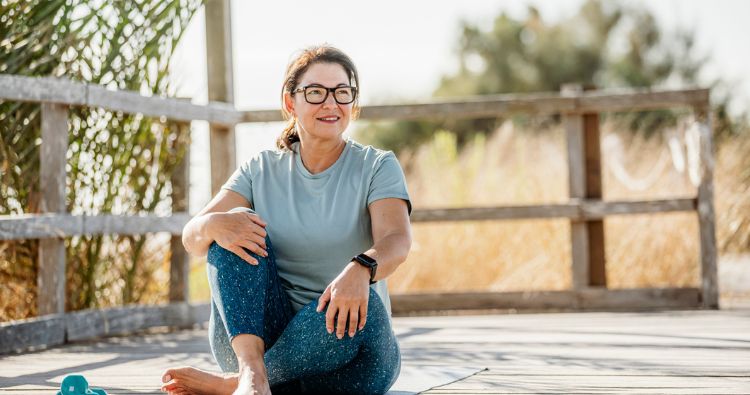 A woman sits on a dock in yoga gear getting ready to stretch.