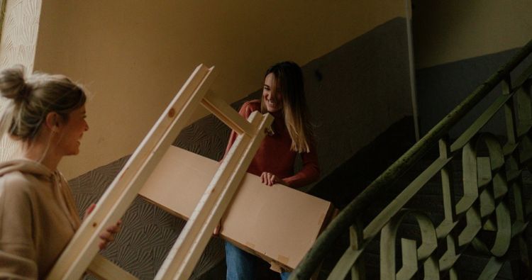 A mother helps her daughter move furniture up the stairs.