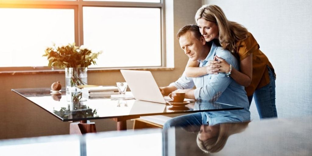 An older white couple embrace while looking at their computer.