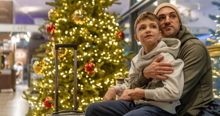 A father and sun sit patiently in an airport in front of a Christmas tree.