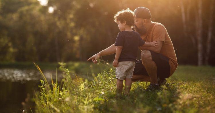 A father ponds out fish in a pond to his young son.