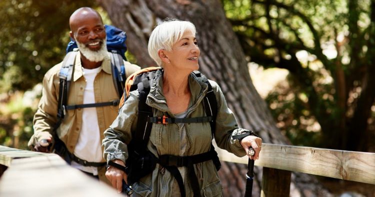 A retired couple walk on a wooden bridge in the woods.