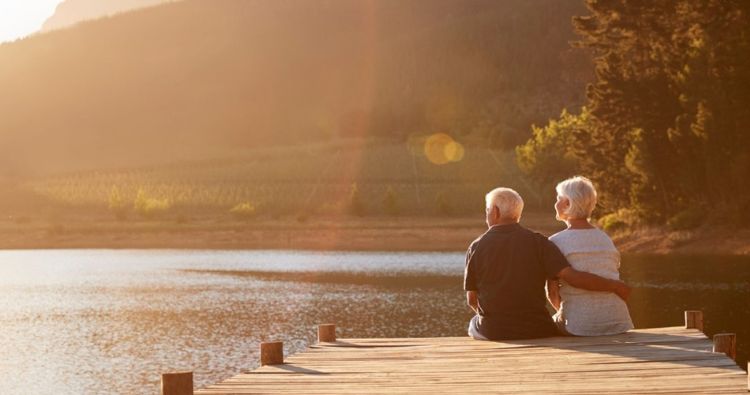 A retire couple watch the sunset off a dock.