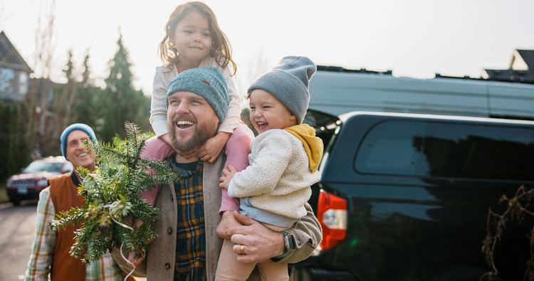 A father carries his young daughter from the car while brining in holiday decorations.